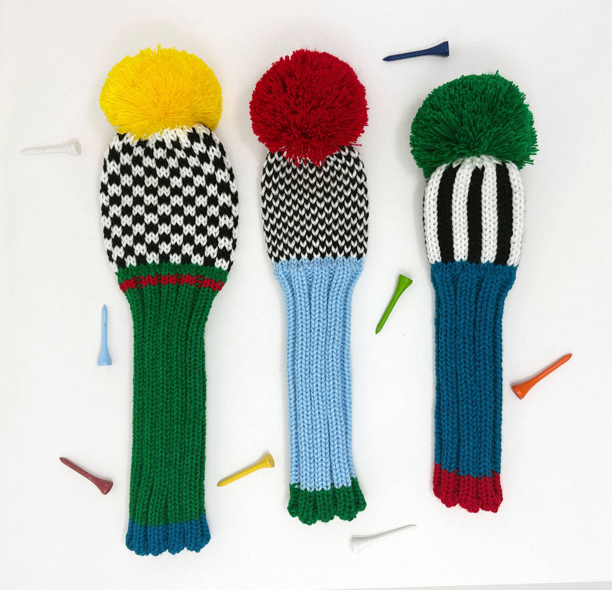 Three knitted golf club covers with colorful pom-poms on a white background