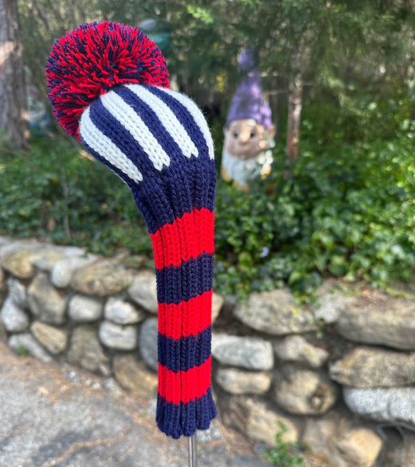 Knitted golf club head cover with red, white, and blue pattern against a garden background