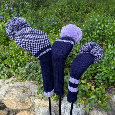 Three knitted golf club covers with pom-poms on a natural background
