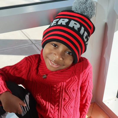 A child wearing a red sweater and a black, red, and white striped beanie with a pom-pom on top.